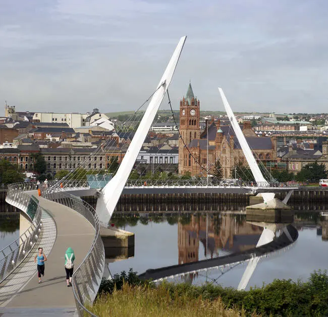 White curved pedestrian bridge spanning river with historic church tower reflected below