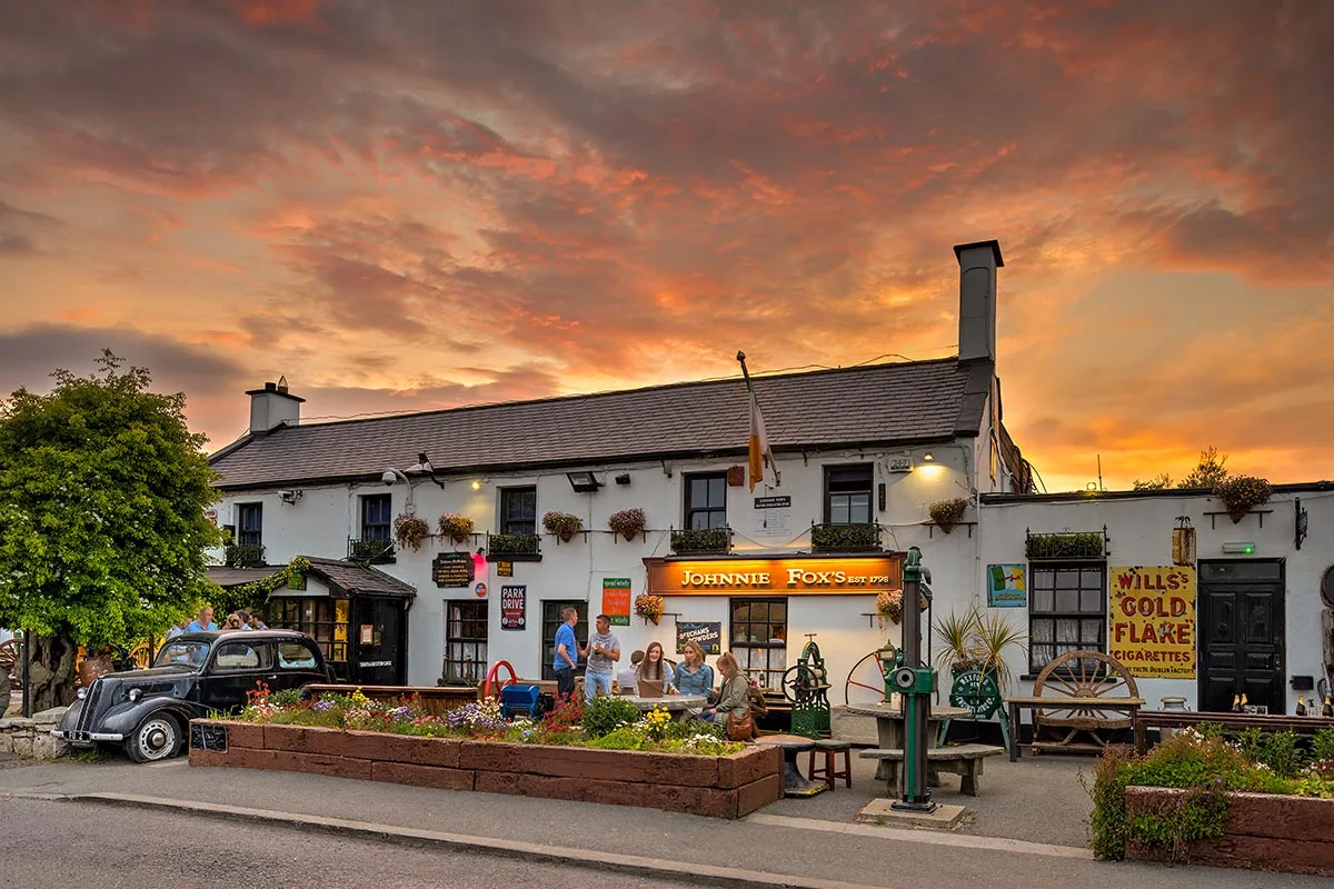 Historic whitewashed Irish pub with golden sunset sky and vintage car parked outside