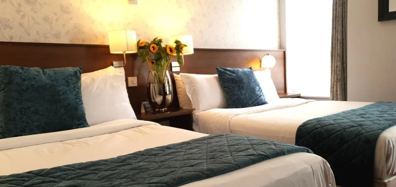 Two beds with white linens and teal accent pillows in hotel room