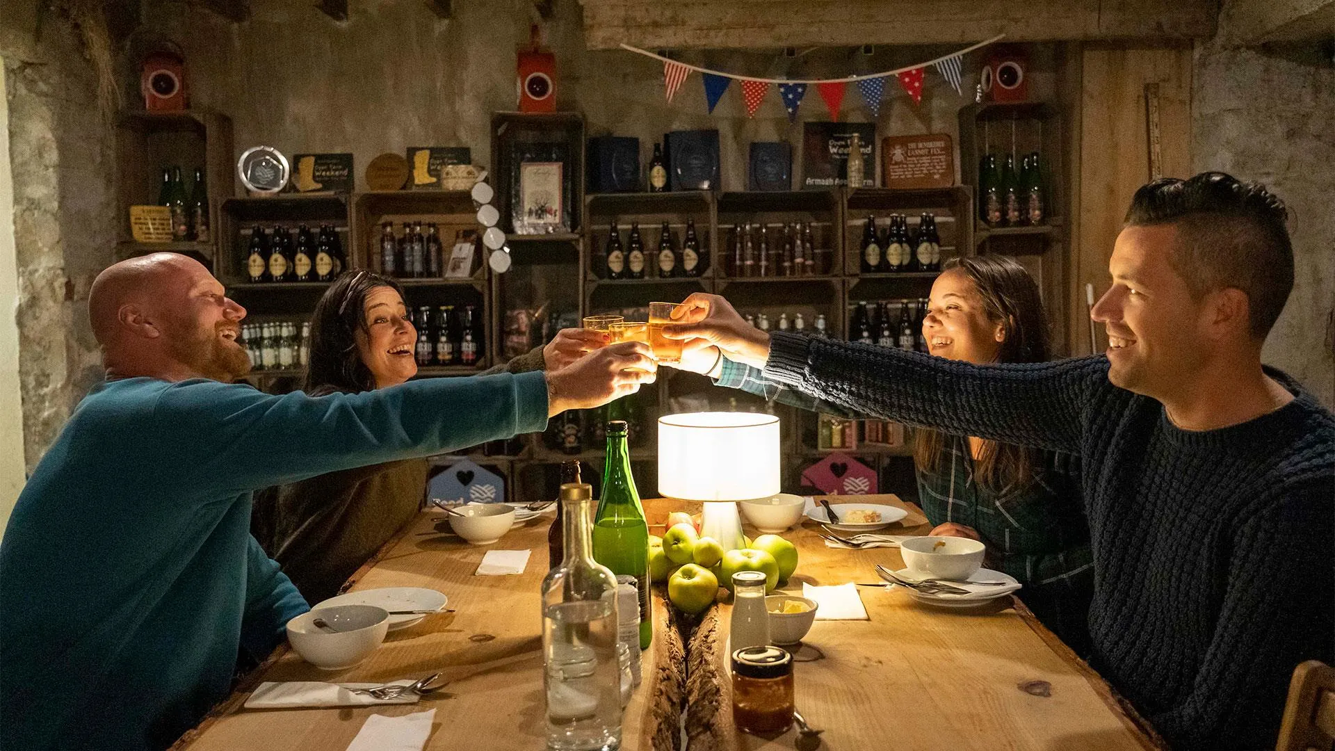 Four people toasting with beer glasses at a wooden table in a rustic pub interior