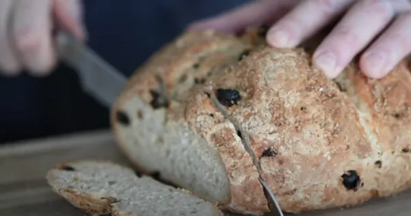 Hands breaking fresh soda bread with dark seeds on wooden surface