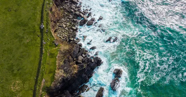 Aerial view of rugged Irish coastline with emerald grass, rocky outcrops, and turquoise waves