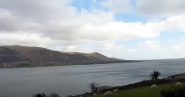 Mountainous coastline with calm bay waters under cloudy sky, Irish landscape