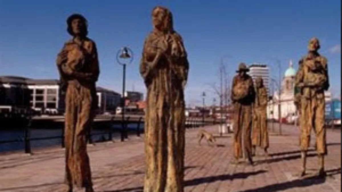 Five bronze statues of figures standing on a waterfront promenade overlooking a harbor