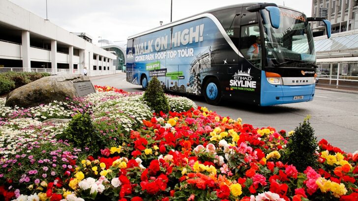 Blue tour bus parked beside vibrant flower garden in urban plaza