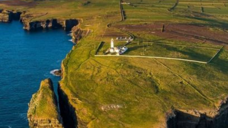 Aerial view of a lighthouse on Irish coastal cliffs with green fields