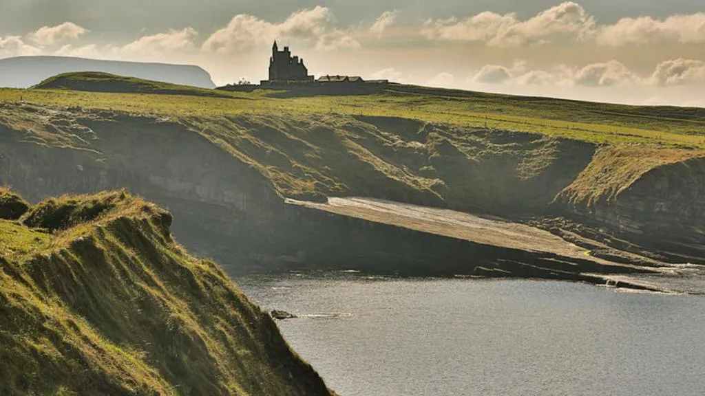 Dramatic coastal canyon with moss-covered cliffs and castle ruins on distant plateau