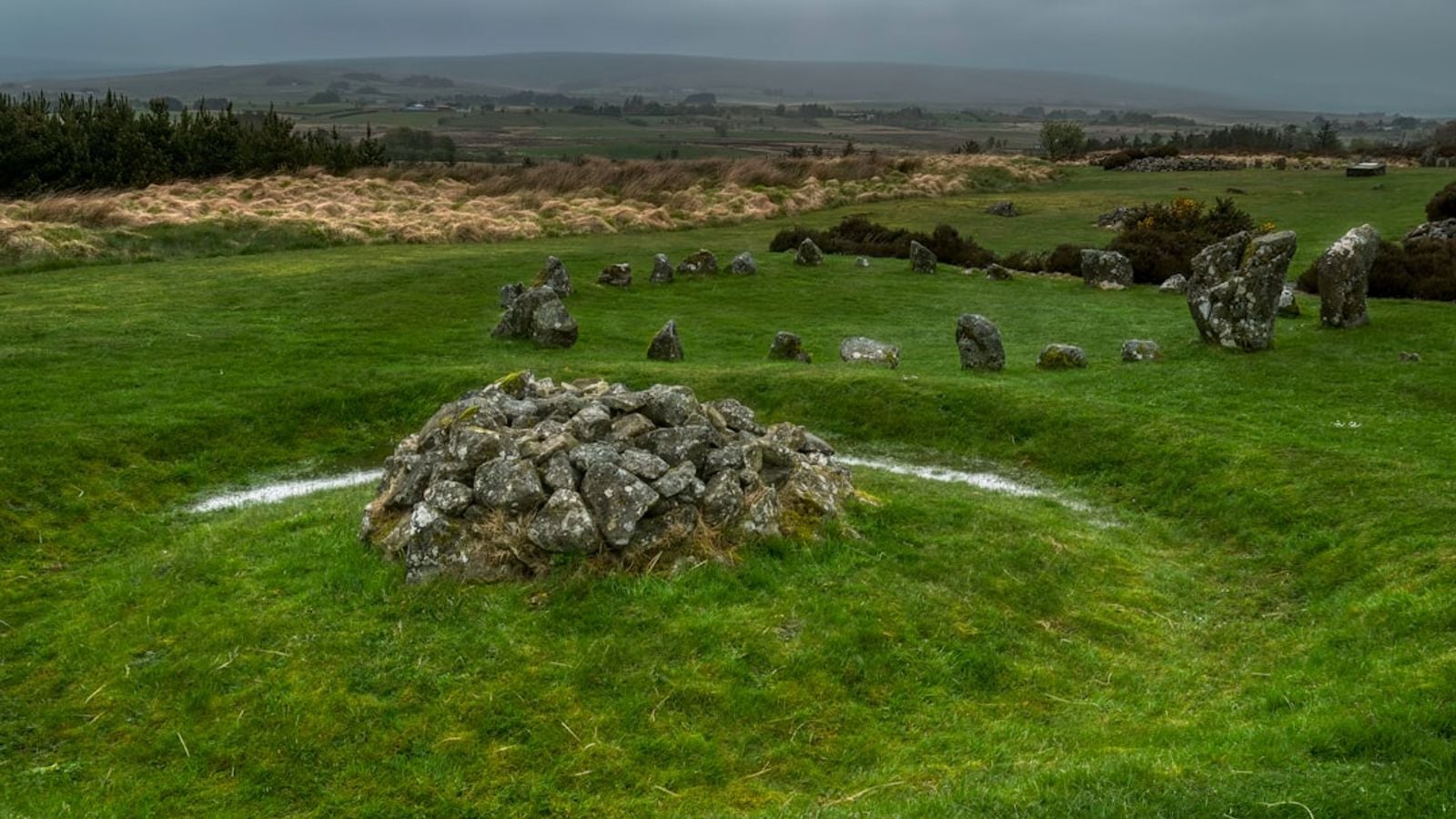 Ancient stone cairn and standing stones on green Irish bogland under a dramatic grey sky