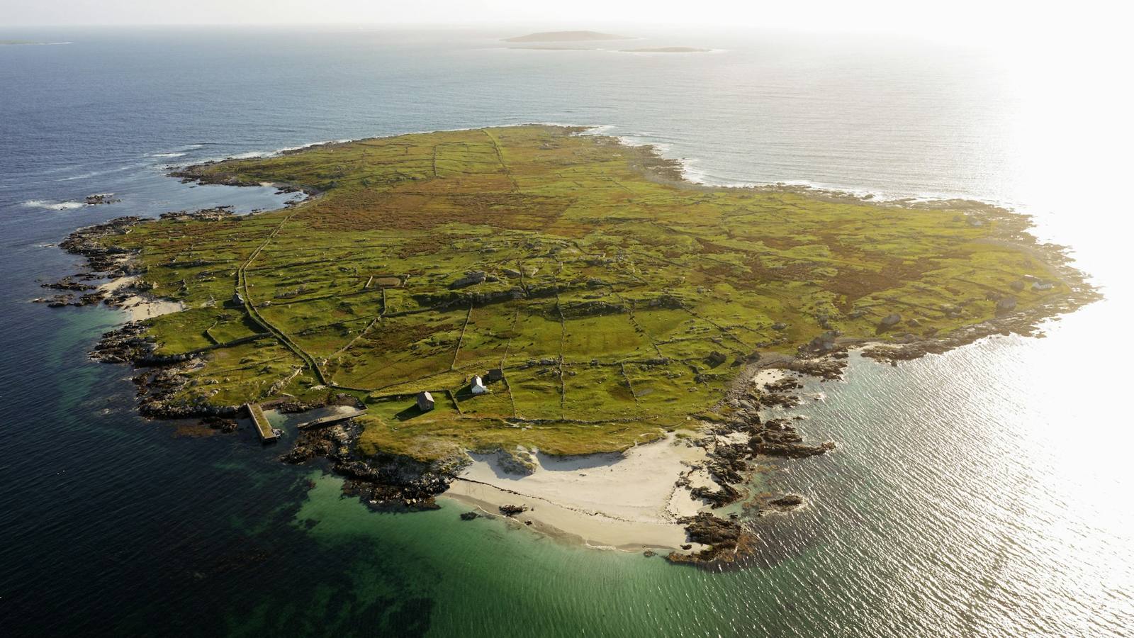 Aerial view of a remote Irish island off the Donegal coast with patchwork green fields stone walls cottages and turquoise Atlantic waters