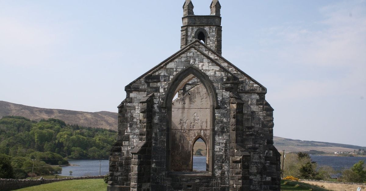 Ruined stone church with large Gothic window overlooking a loch