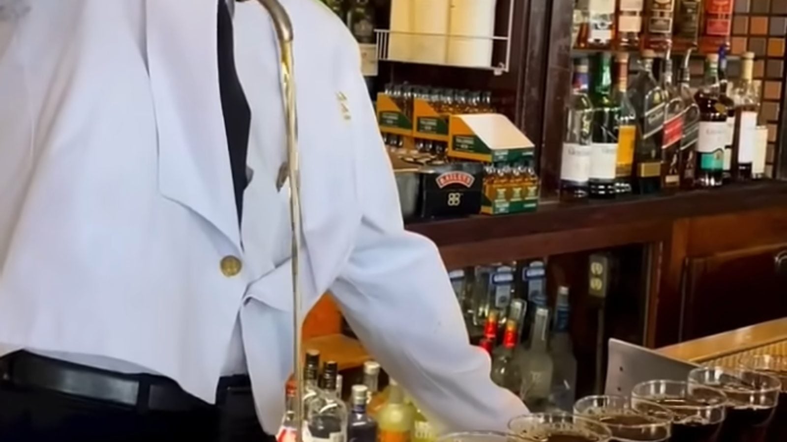 A bartender pouring Irish whiskey into a row of Irish coffee glasses at a pub bar