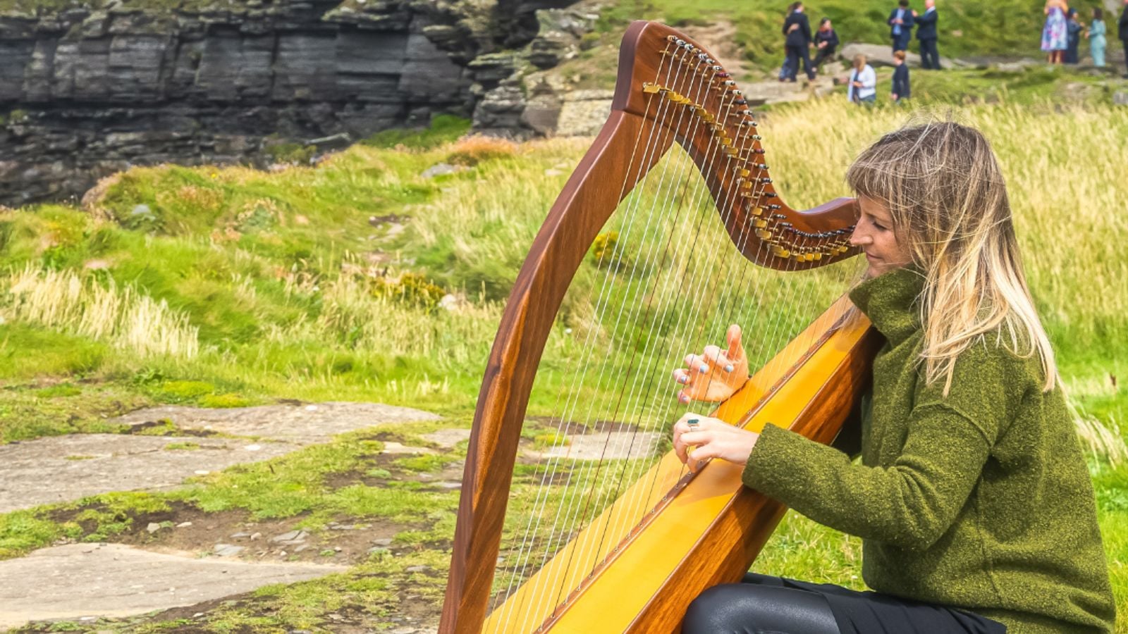 A woman playing a traditional Irish harp outdoors in an Irish landscape with a stone tower