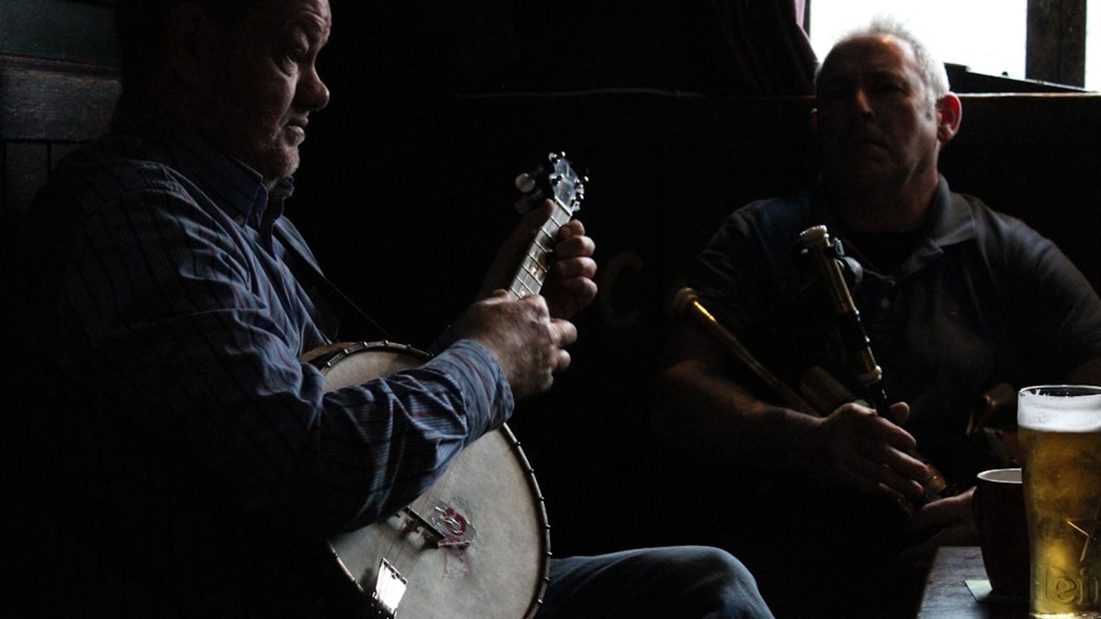 Two musicians playing banjo and uilleann pipes at an Irish traditional music session in a pub