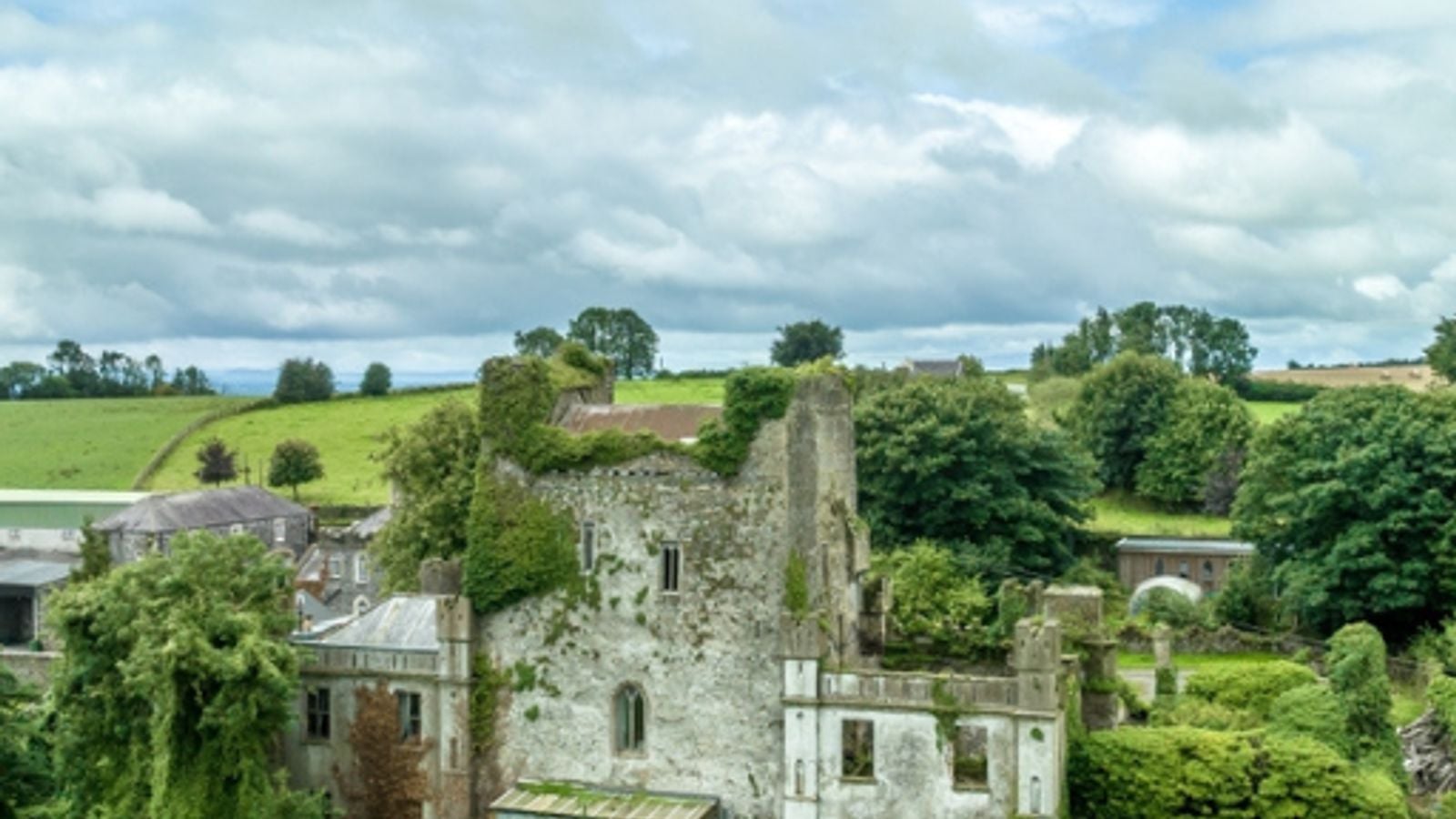 Aerial view of the ruined Leap Castle in County Offaly, Ireland, its walls overgrown with ivy and surrounded by green countryside