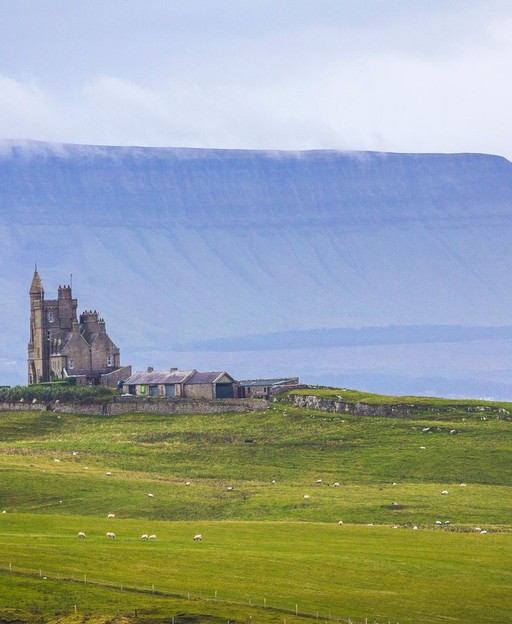 Castle ruins on green hillside with dramatic mountain backdrop in Ireland
