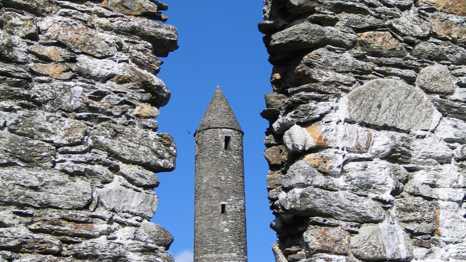 The round tower at Glendalough framed through an ancient stone archway in County Wicklow, Ireland