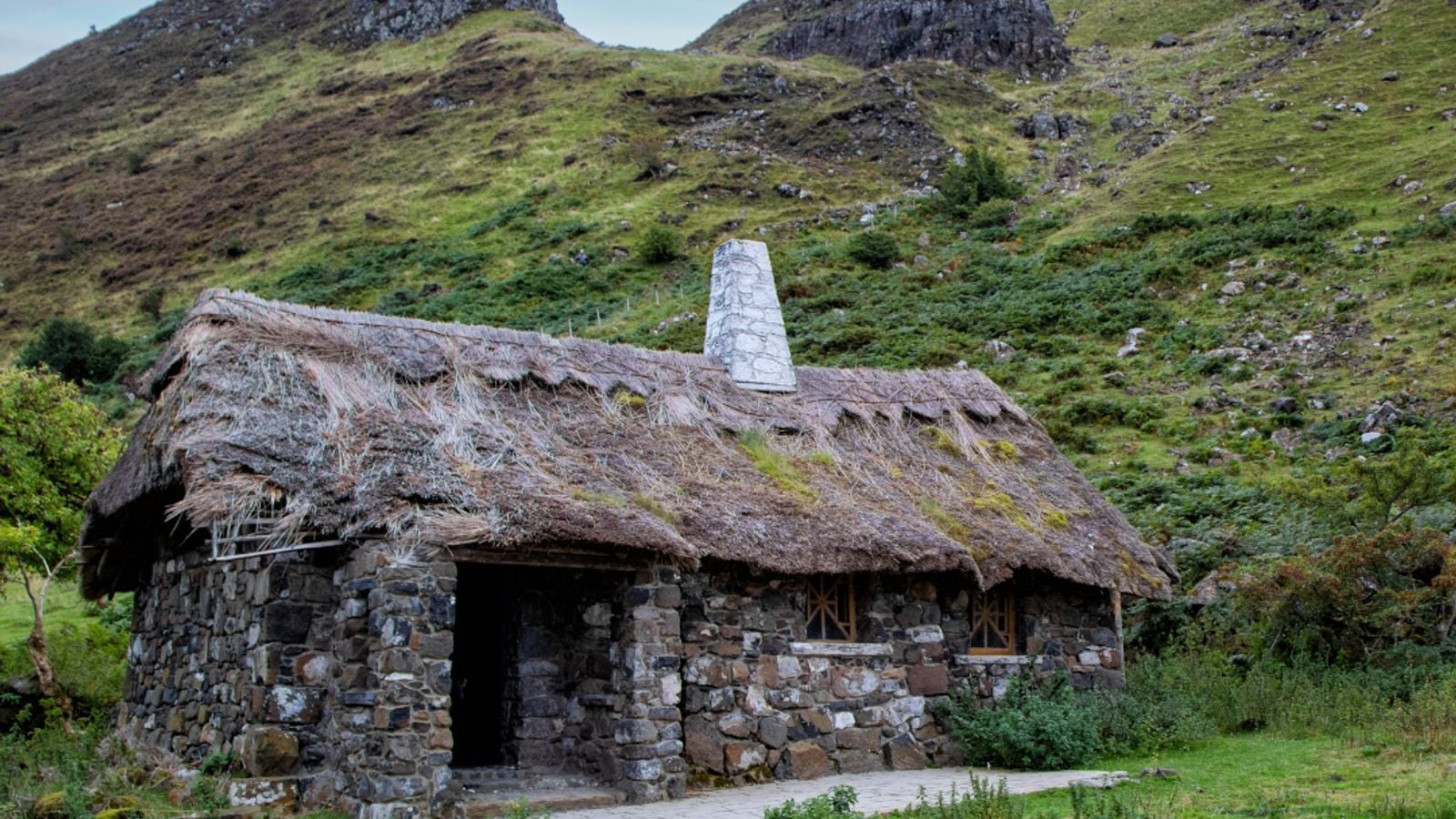 Traditional Irish thatched stone cottage with stone chimney nestled in a mountain valley in County Kerry, Ireland