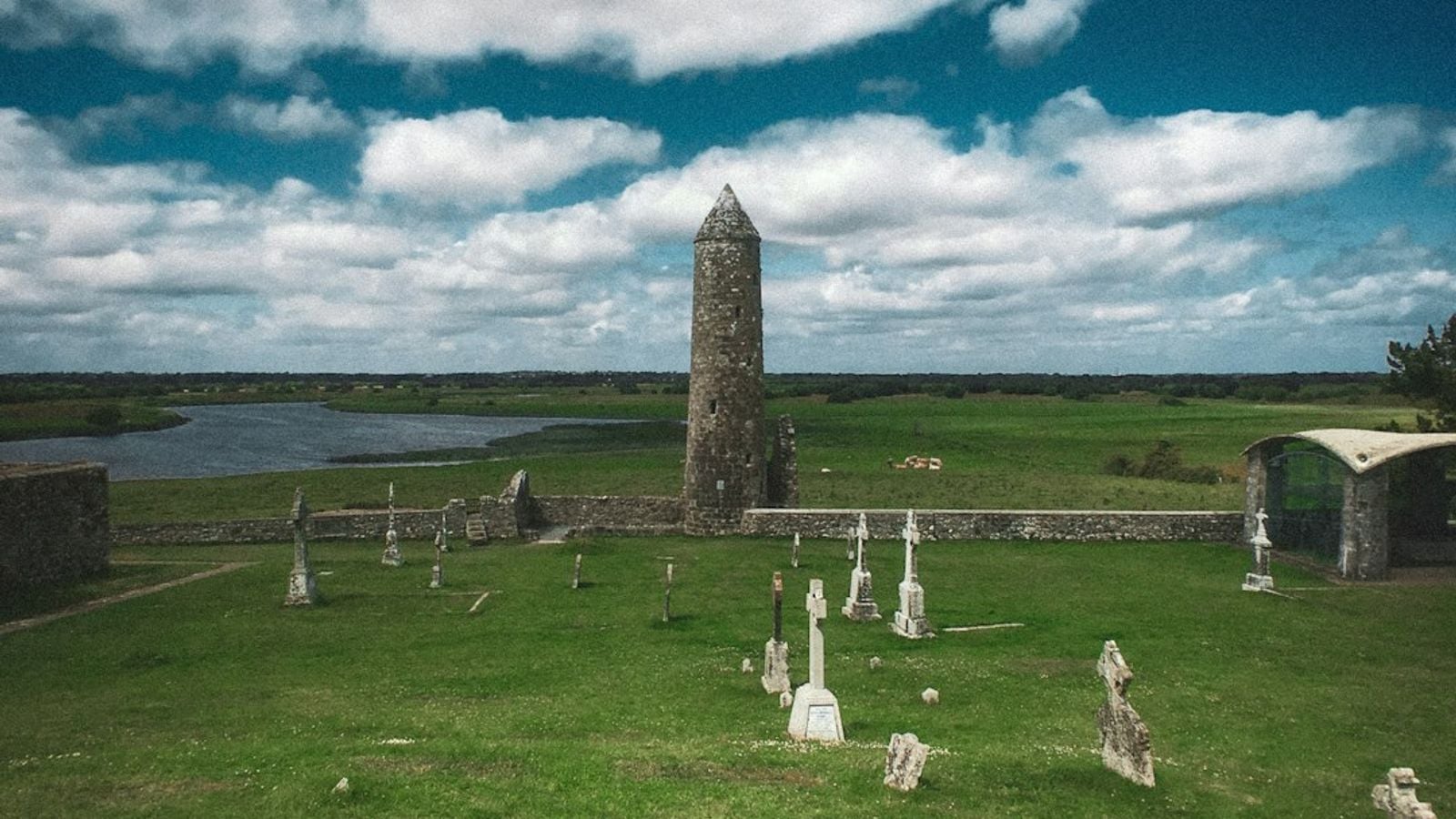 Clonmacnoise round tower rising above ancient gravestones beside the River Shannon, County Offaly, Ireland