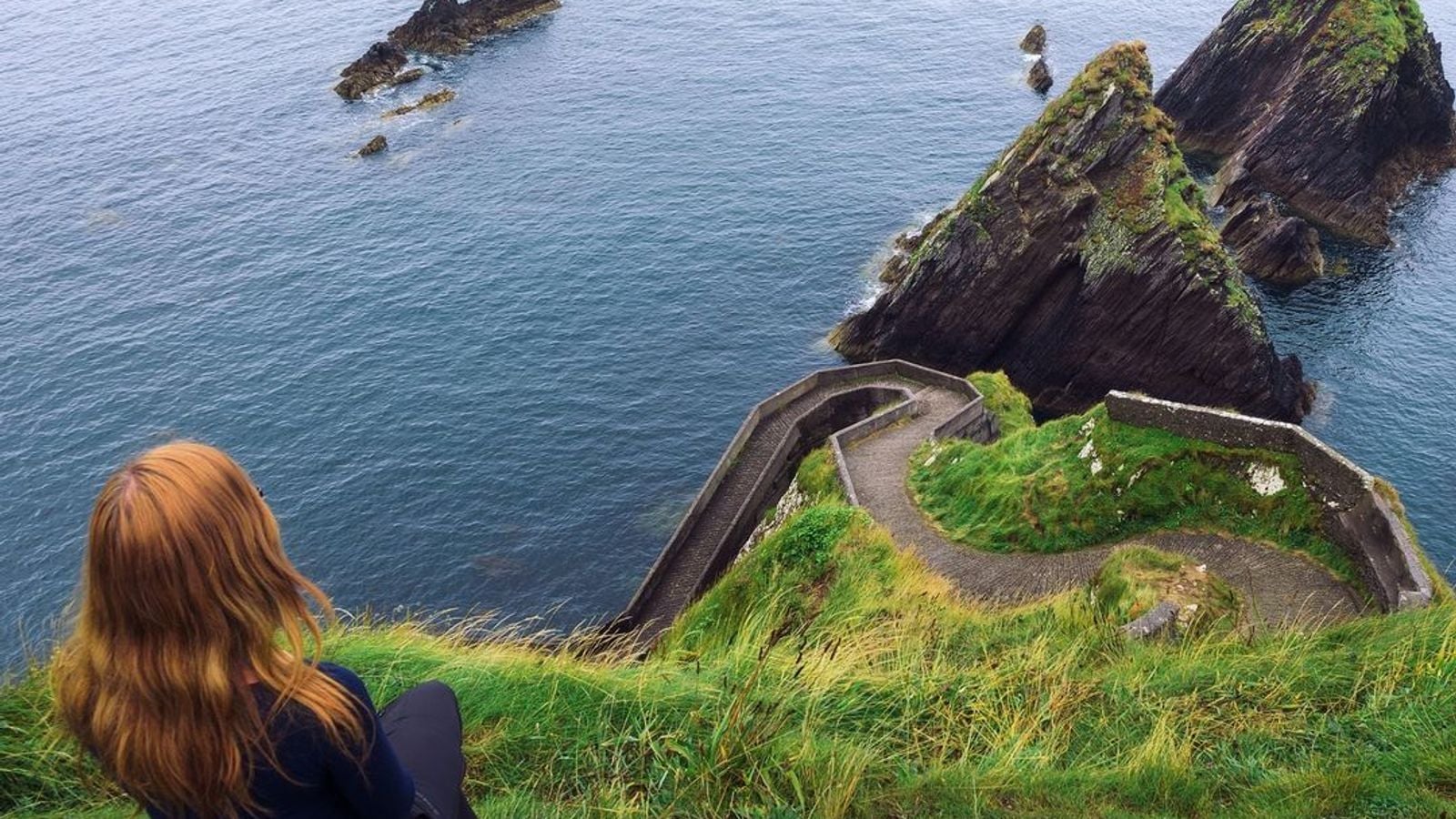 Woman looking out from the cliffs at Dunquin Pier on the Dingle Peninsula, Kerry, with the wild Atlantic Ocean below