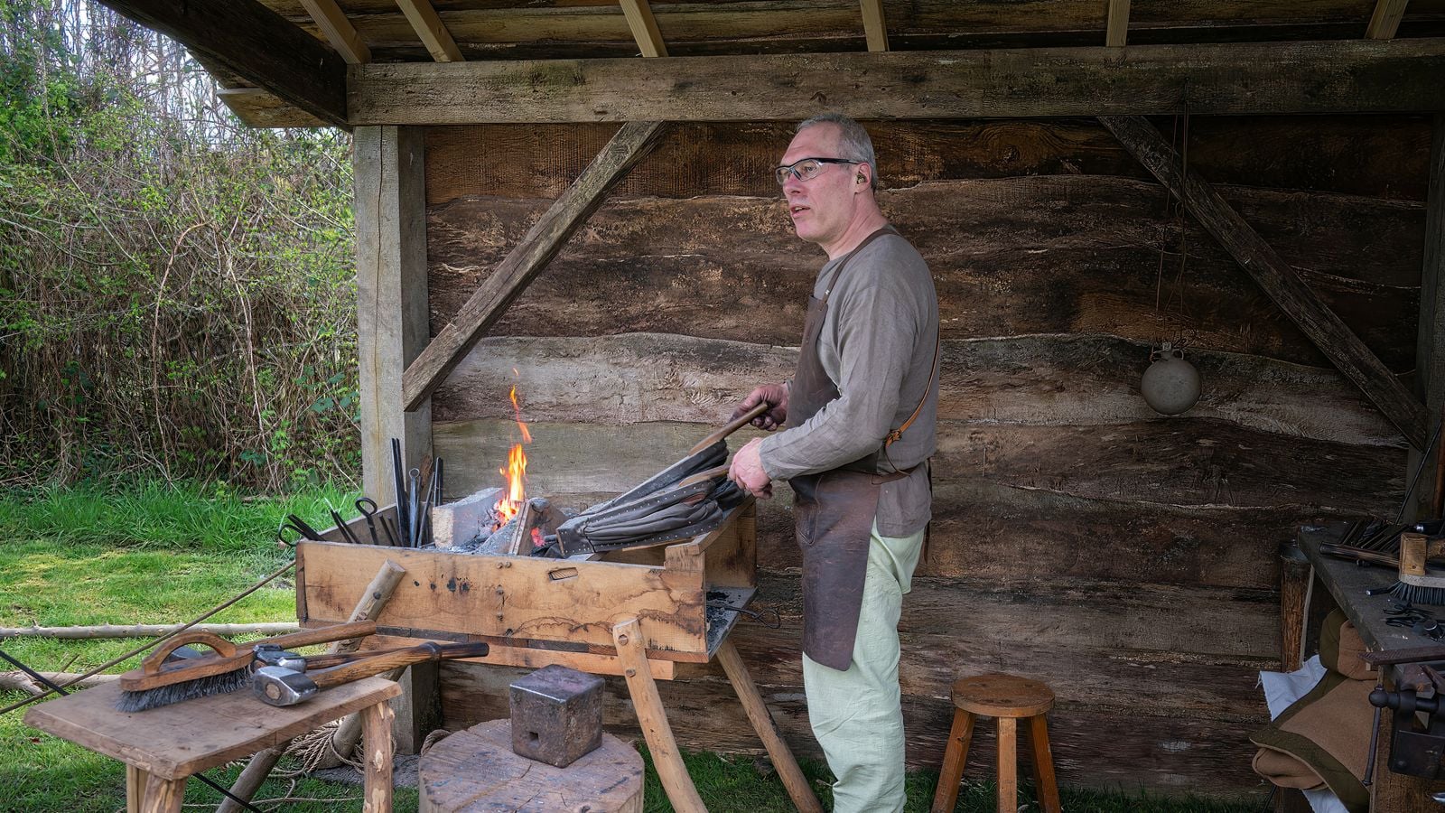 A blacksmith at work in a traditional forge, tending to fire and iron tools
