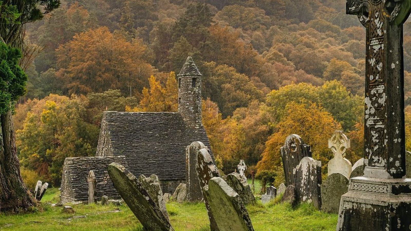 Ancient Celtic cross standing among weathered gravestones in Glendalough monastic cemetery, County Wicklow