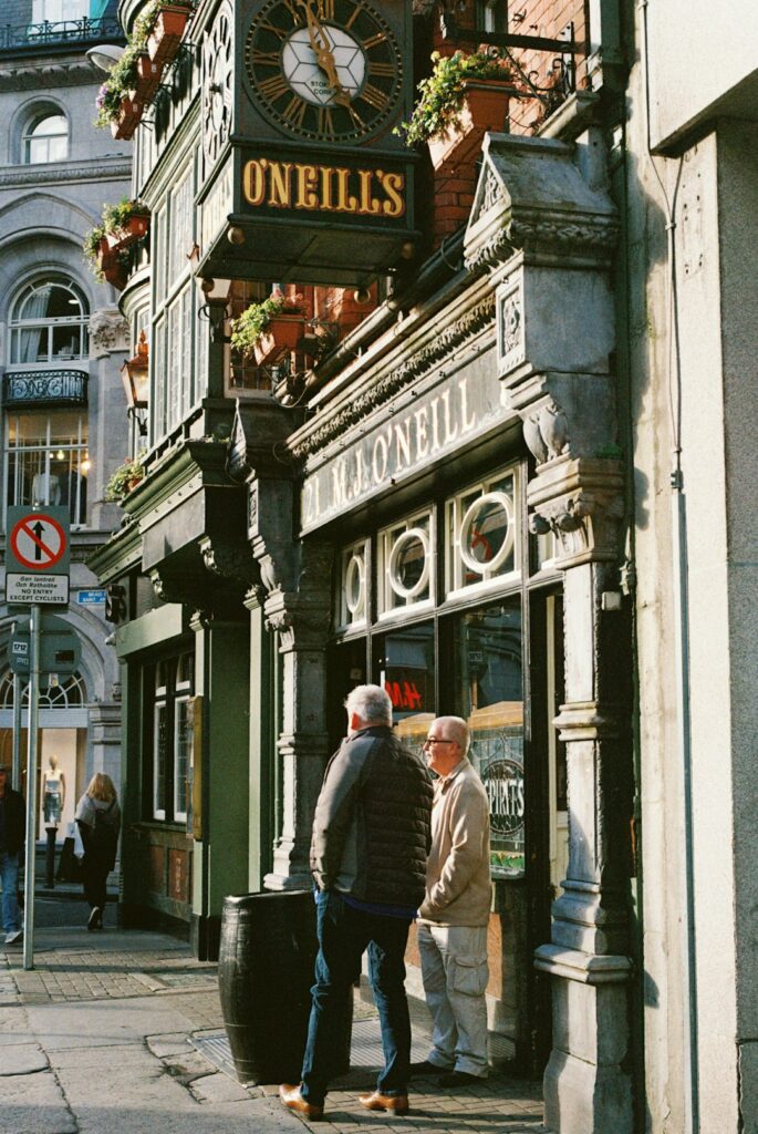 Two men standing outside O'Neill's pub storefront on a Dublin street