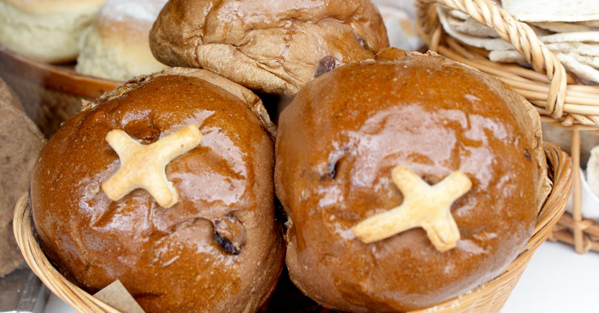 Golden brown hot cross buns with white flour crosses on top, nestled in a woven basket, freshly glazed and ready to serve