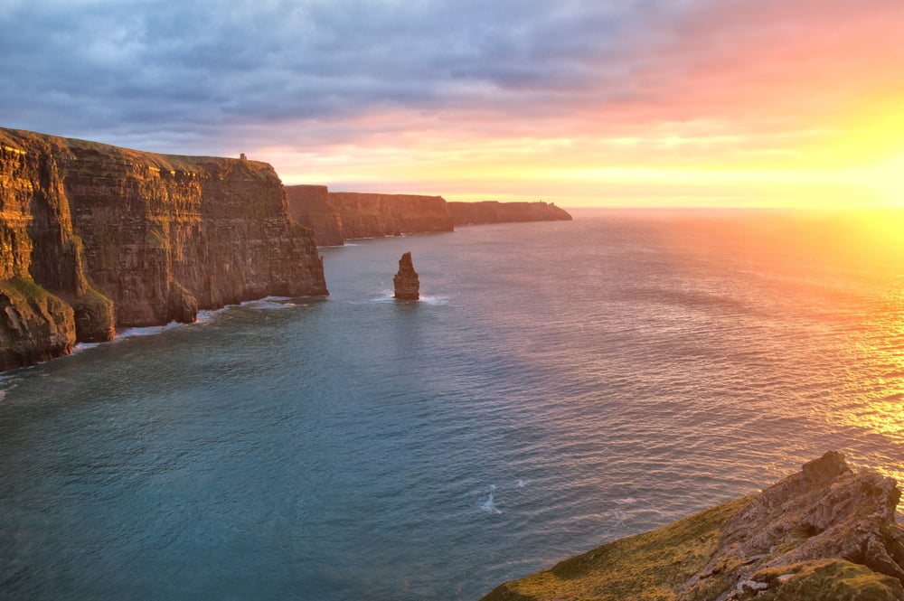 Dramatic coastal cliffs at sunset with isolated rock stack and golden ocean light