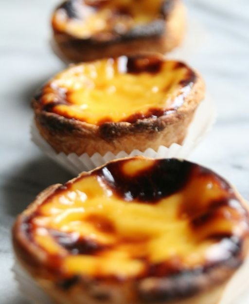Three golden past&eacute;is de nata (Portuguese custard tarts) with flaky pastry and caramelised egg custard filling