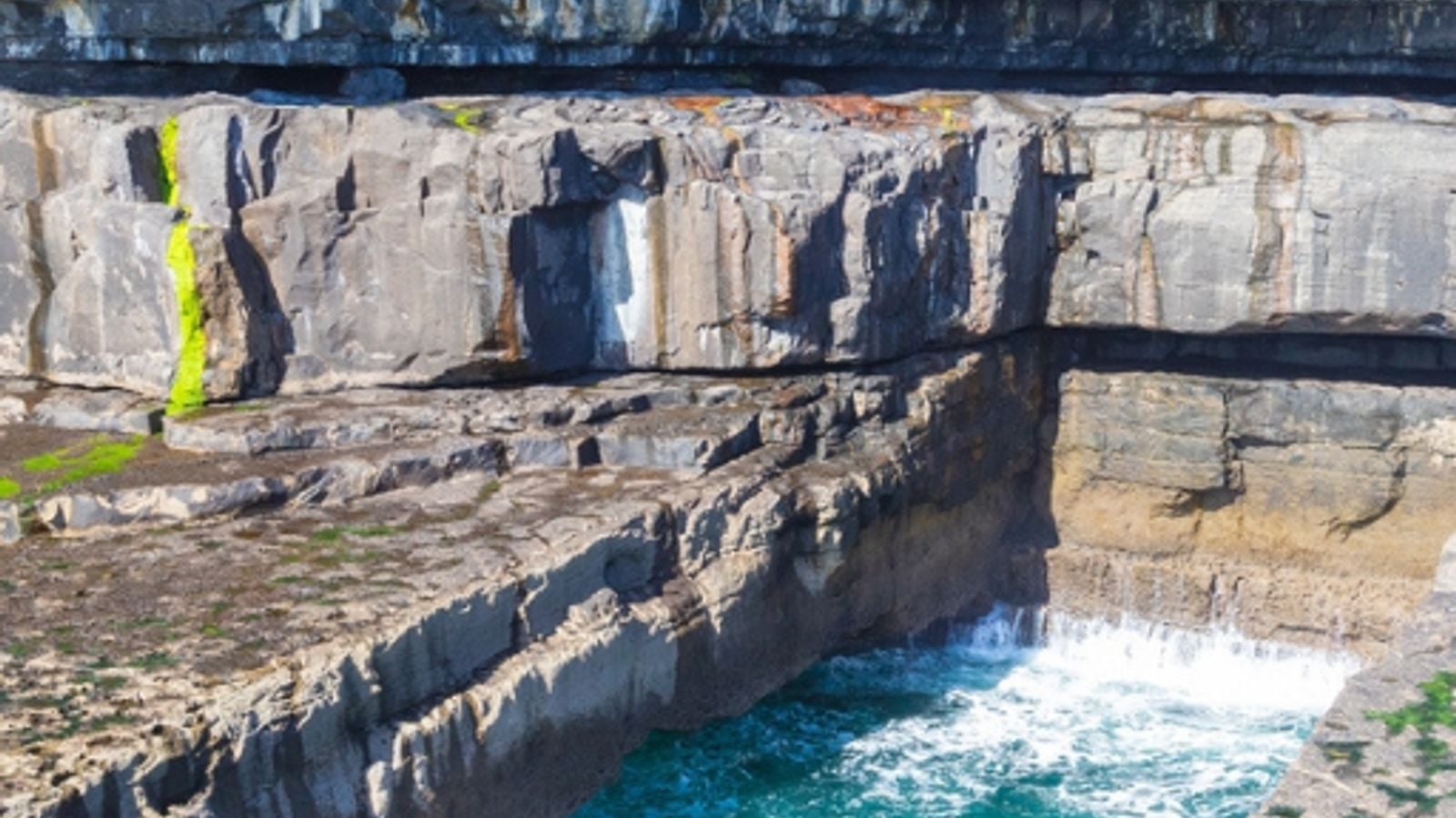 The turquoise waters of Poll na bP&eacute;ist, the Wormhole on Inis M&oacute;r, Aran Islands, carved into grey limestone