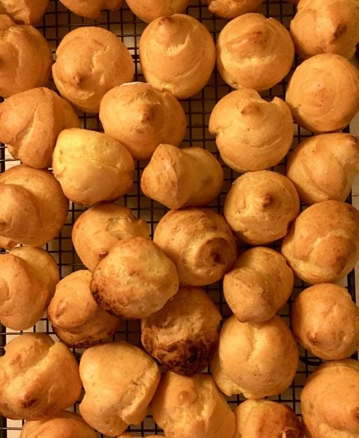 Freshly baked golden choux pastry puffs cooling on a wire rack ready to fill