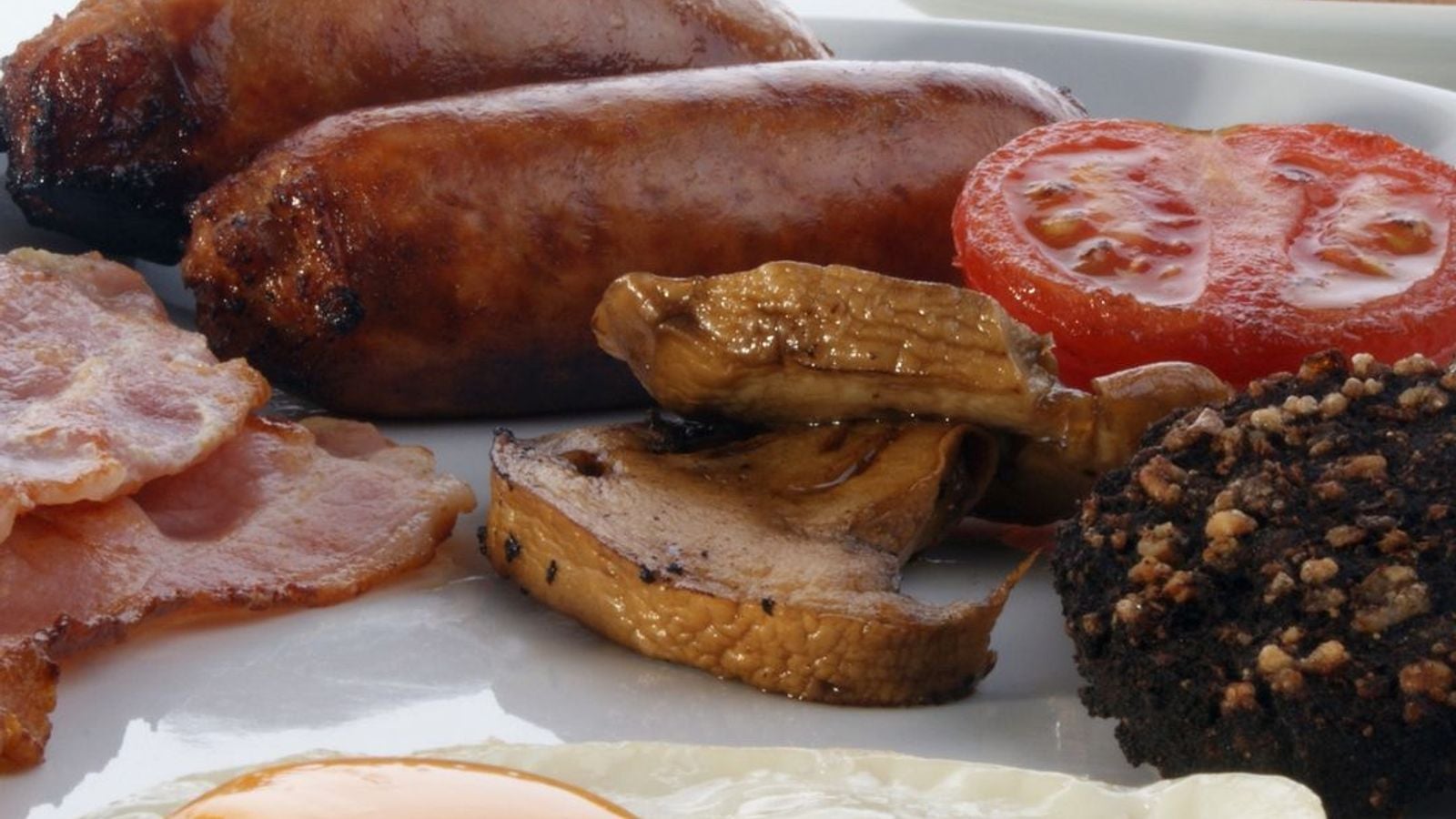 A full Irish breakfast with rashers, sausages, fried egg, black pudding, grilled tomato and mushrooms on a white plate