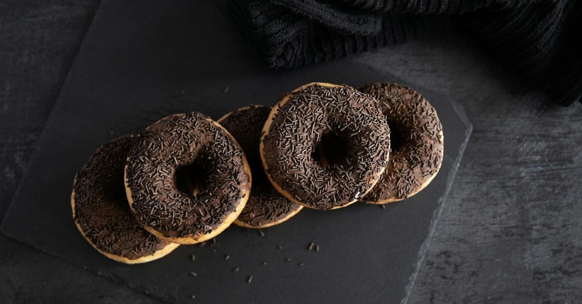 Five chocolate-glazed ring doughnuts with sprinkles on a dark slate surface