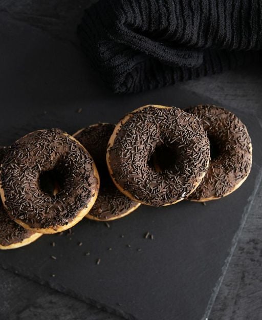Five chocolate-glazed ring doughnuts with sprinkles on a dark slate surface