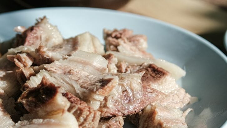 Shredded cooked meat on a white plate with wooden table and bowl in background