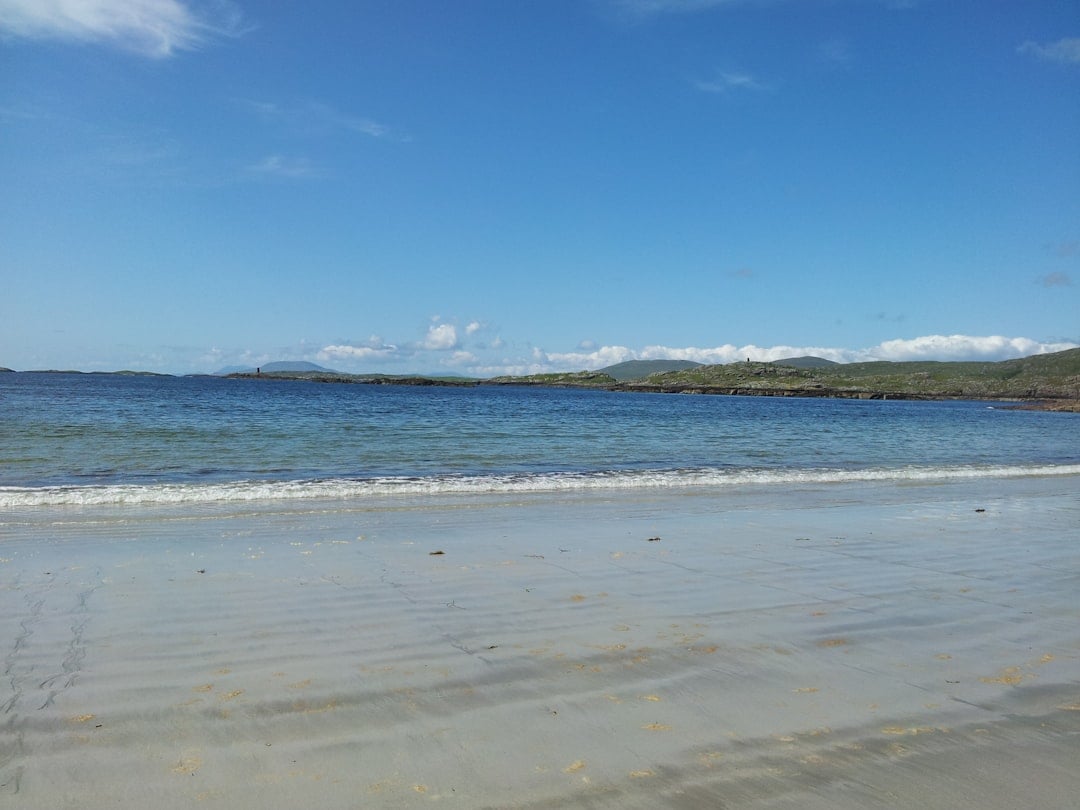 Sandy beach with gentle waves and green hills across calm blue water