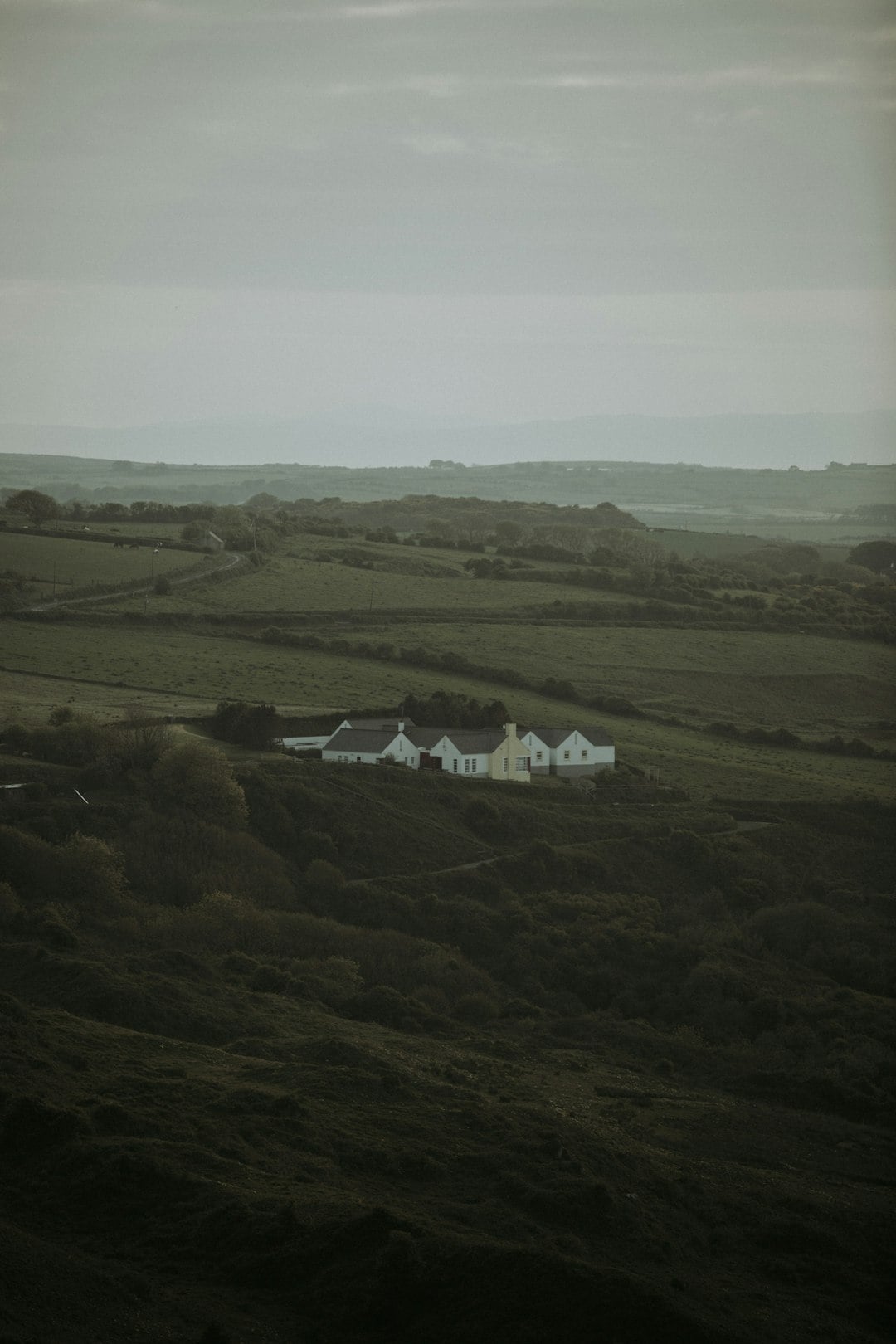 White farmhouse nestled in rolling green hills under overcast sky