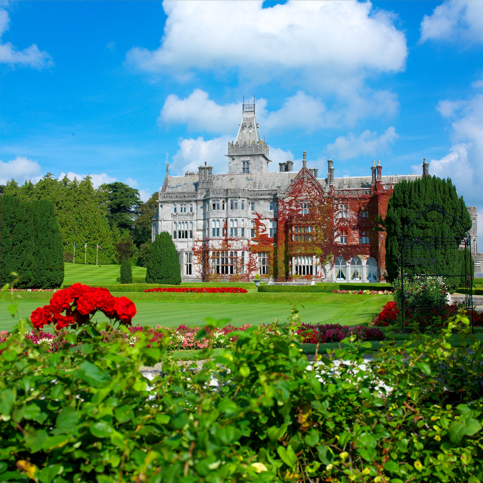 Adare Manor's ivy-covered Gothic Revival facade viewed across manicured gardens and rose beds, County Limerick, Ireland