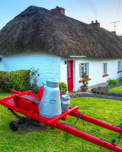 Thatched Irish cottage with red door and milk churn — a classic Irish village scene