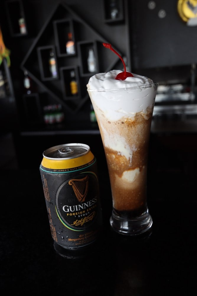 A Guinness ice cream float topped with cream and a cherry, beside a can of Guinness stout