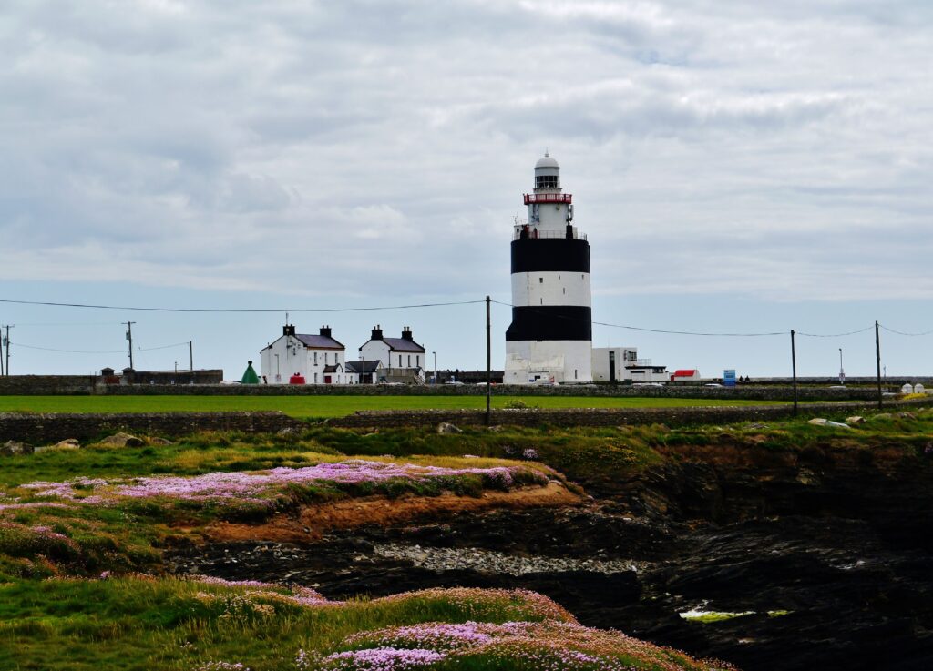 Hook Lighthouse's black-and-white striped tower and keeper's cottages on the Hook Peninsula, County Wexford, seen from across the headland
