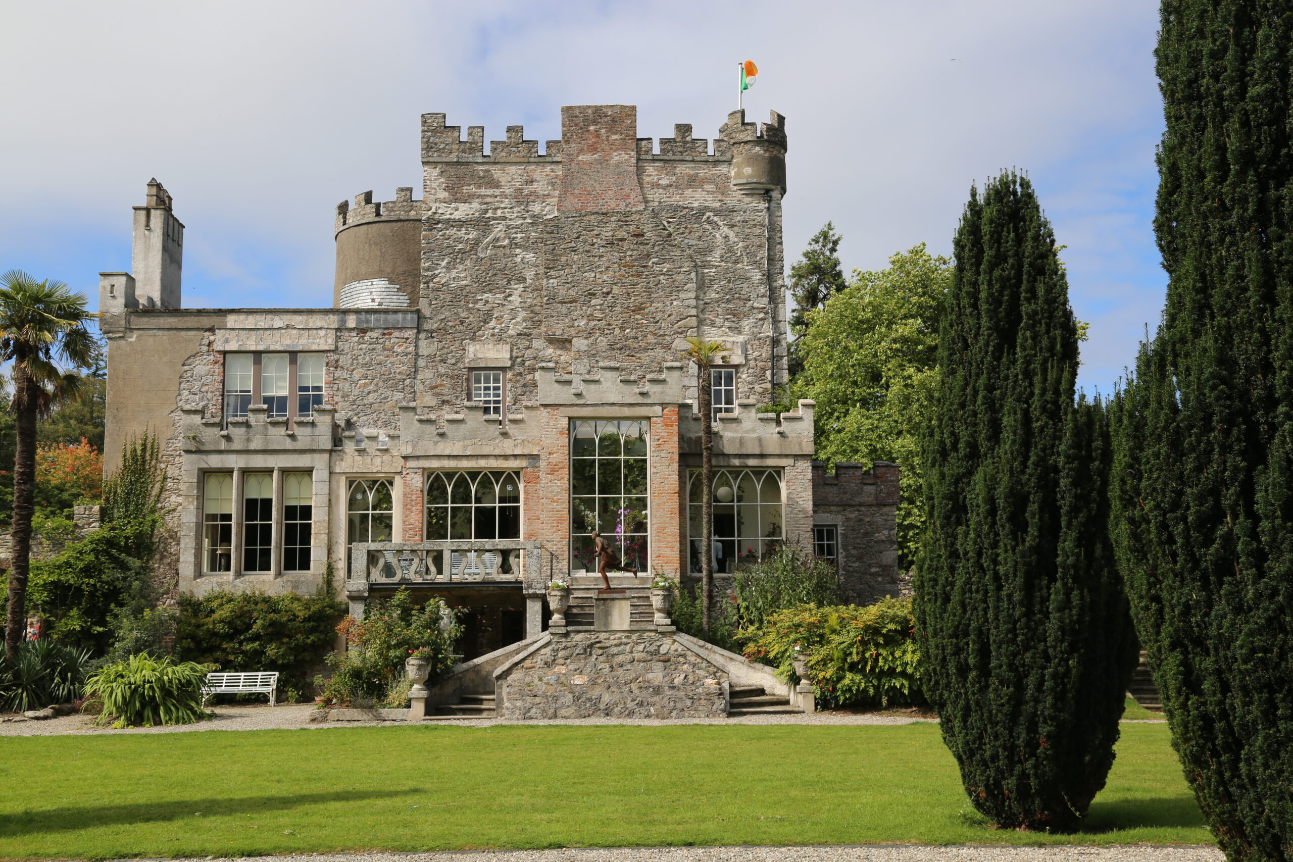 Huntington Castle in Clonegal, County Carlow, seen from the garden, with its crenellated stone tower, round turret flying the Irish tricolour, and a stone staircase leading up to the house