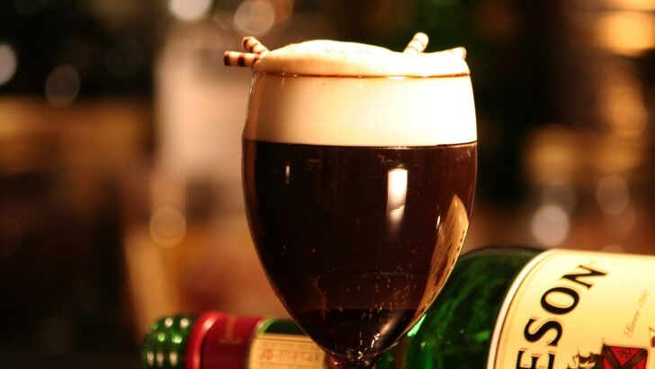 A glass of traditional Irish coffee with a distinct layer of cream floating on top of hot coffee, served beside a bottle of Jameson Irish whiskey