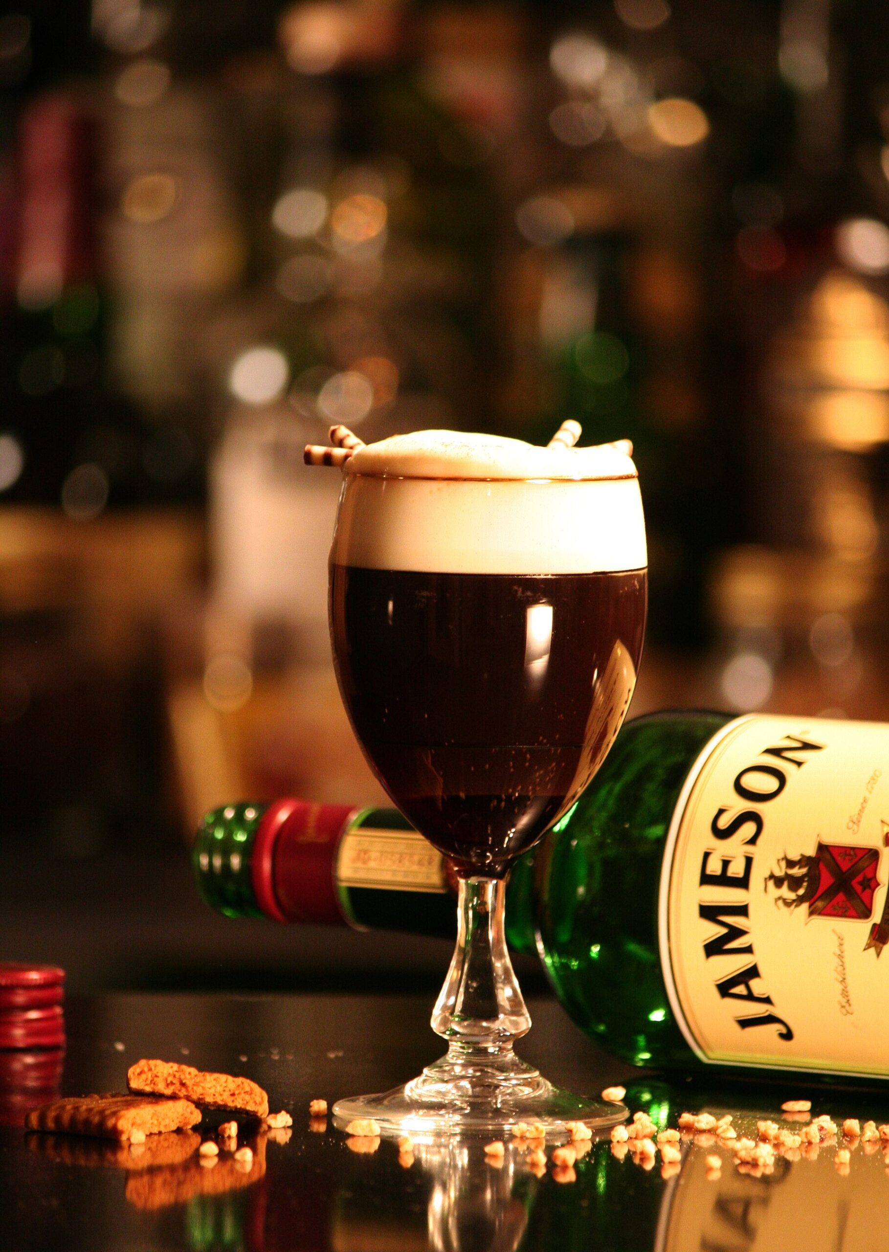 A glass of traditional Irish coffee with a distinct layer of cream floating on top of hot coffee, served beside a bottle of Jameson Irish whiskey