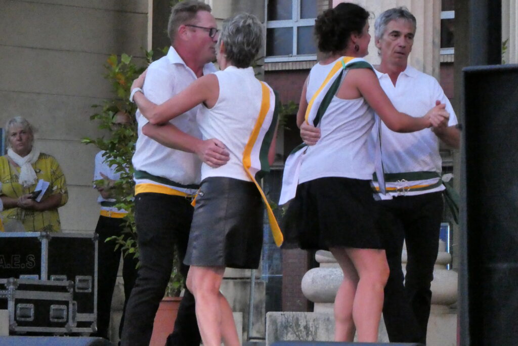 Two couples dancing Irish set dancing in casual dress with green-white-orange sashes at a Celtic cultural festival