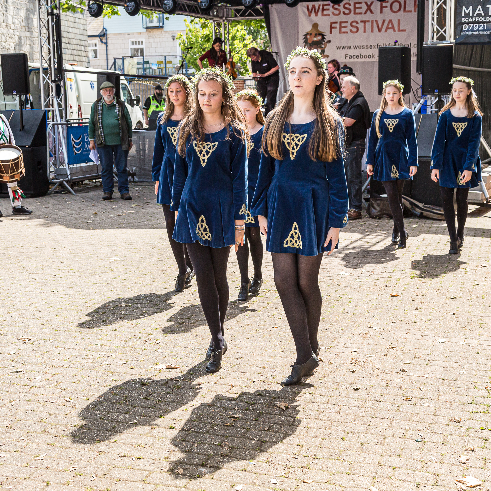 Young Irish dancers in traditional blue dresses with gold Celtic embroidery performing at a folk festival
