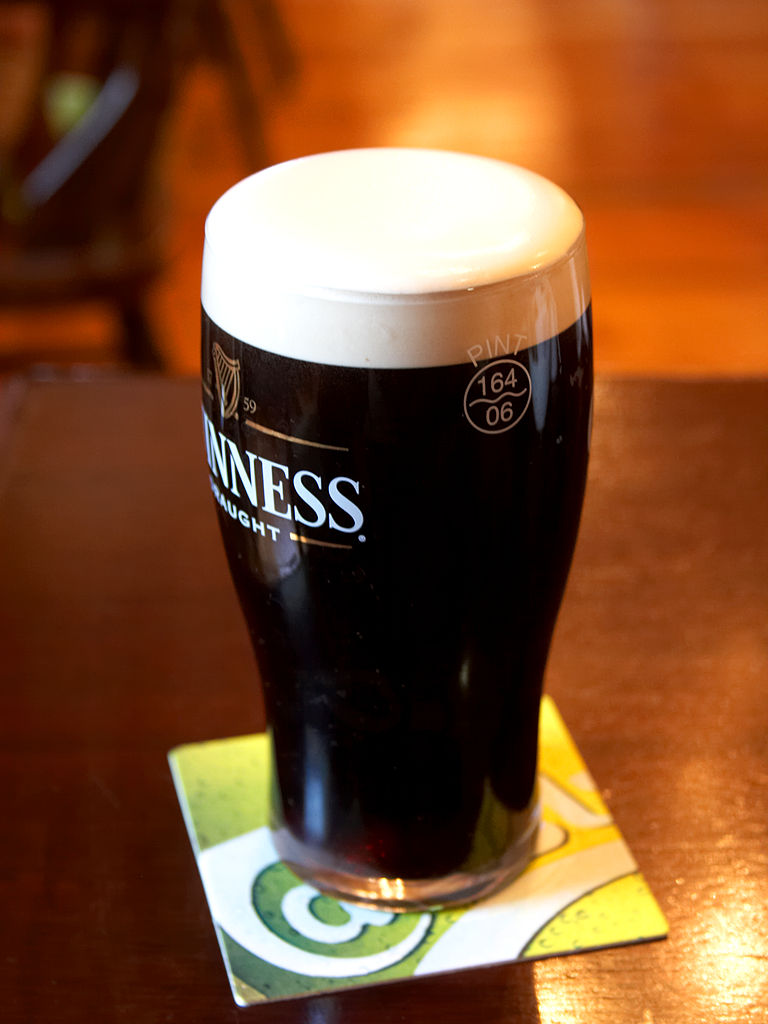 A freshly poured pint of Guinness stout with a thick creamy head, resting on a beer mat on a pub table