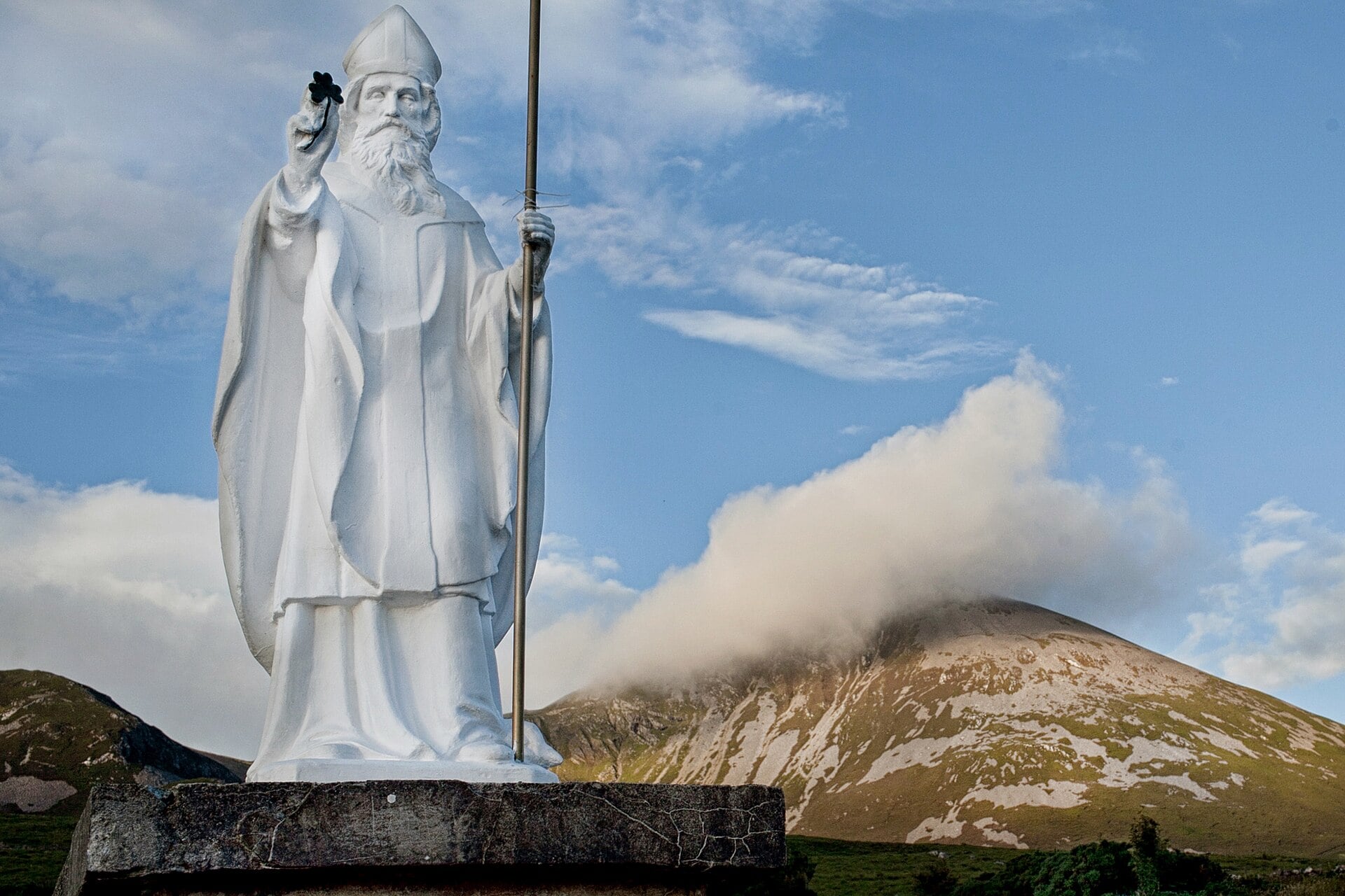 White statue of Saint Patrick at the base of Croagh Patrick, with the cloud-capped mountain behind it