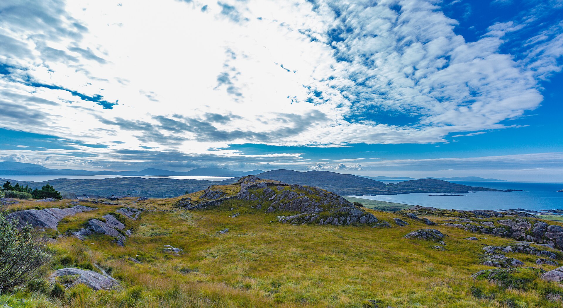 Rocky upland hilltop with a ruined stone enclosure overlooking a bay and distant mountains