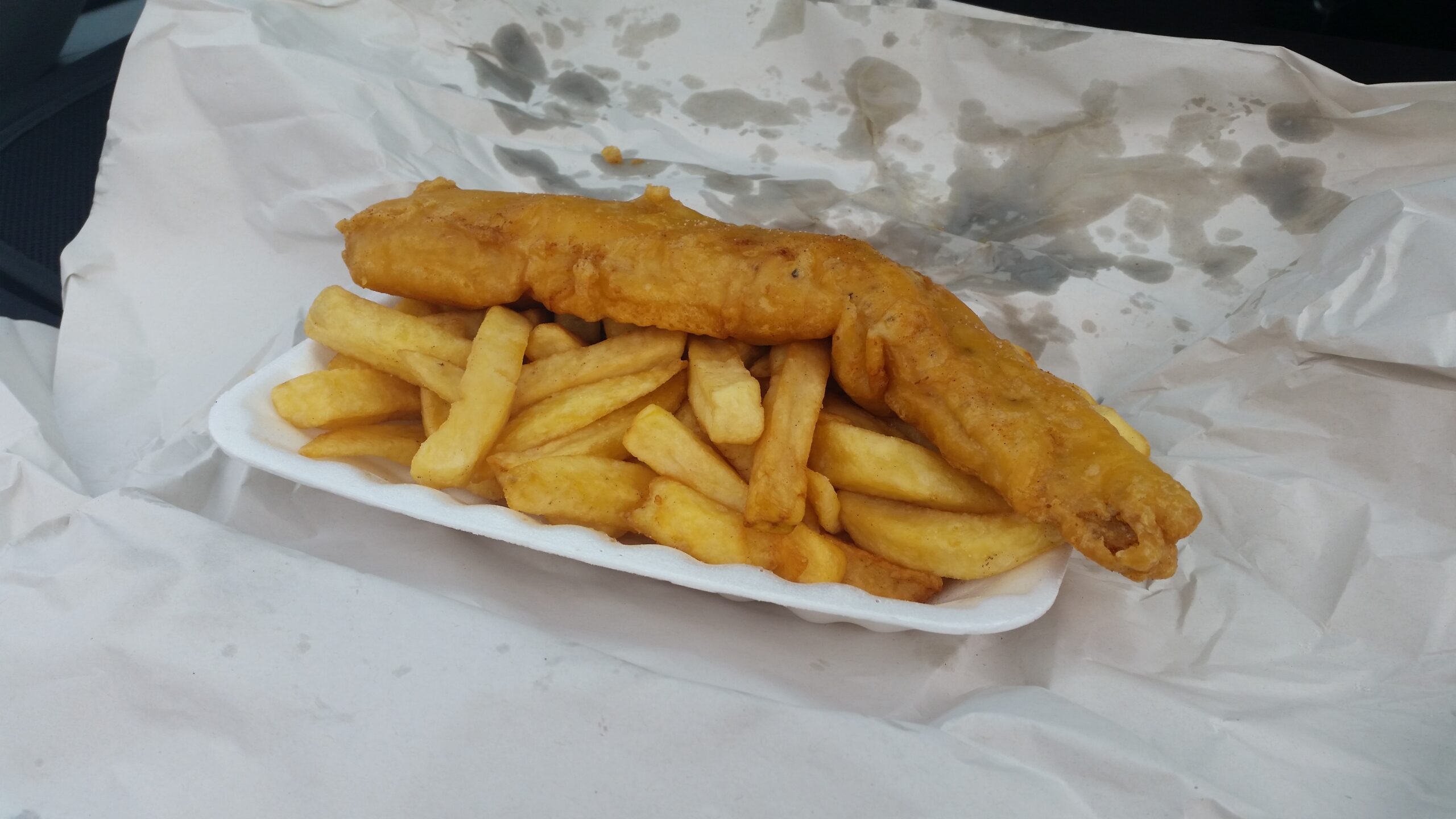 A takeaway tray of golden battered fish and chips wrapped in paper, the classic seaside chipper meal found along Ireland's coast